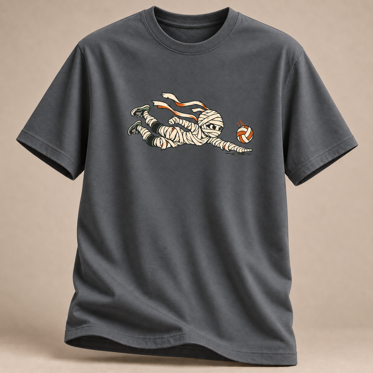 Frontansicht eines anthrazitfarbenen T-Shirts: Mumie beim Hechtbagger mit Volleyball im Halloween-Motiv.