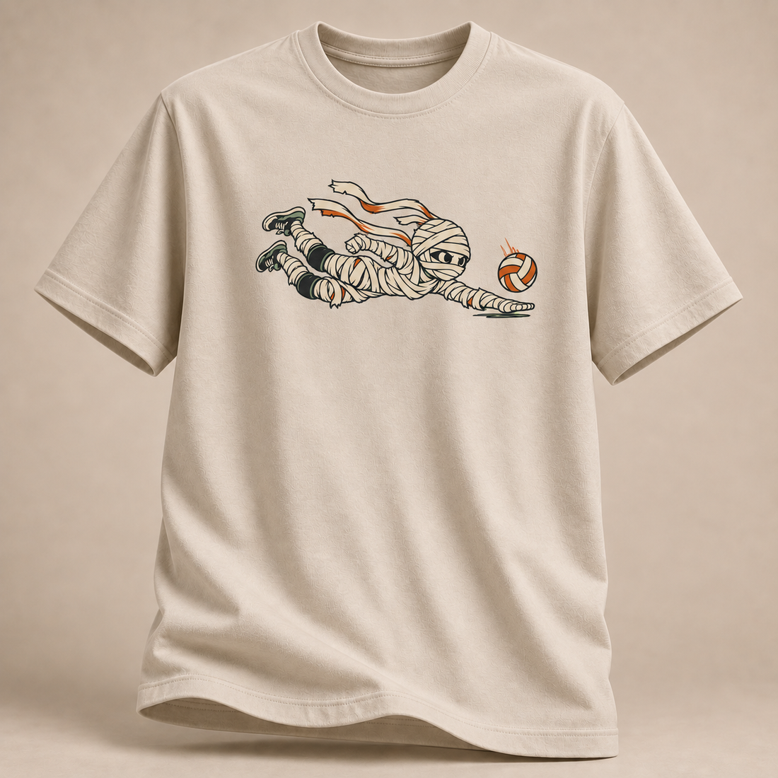 Frontansicht eines sandfarbenen T-Shirts: Mumie beim Hechtbagger mit Volleyball im Halloween-Motiv.