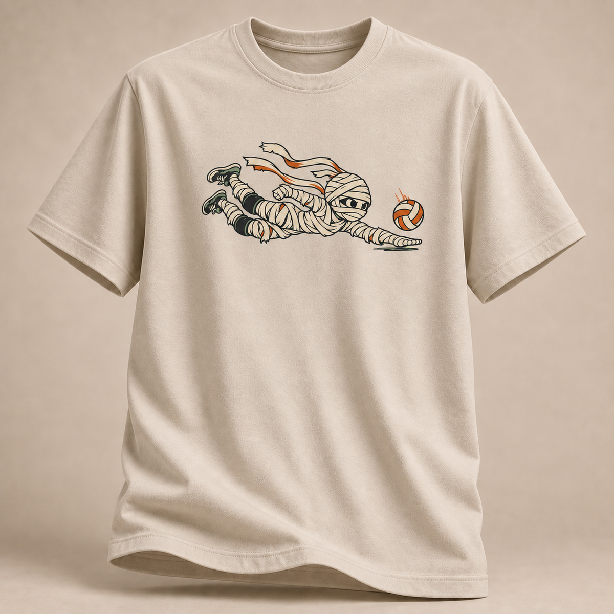 Frontansicht eines sandfarbenen T-Shirts: Mumie beim Hechtbagger mit Volleyball im Halloween-Motiv.